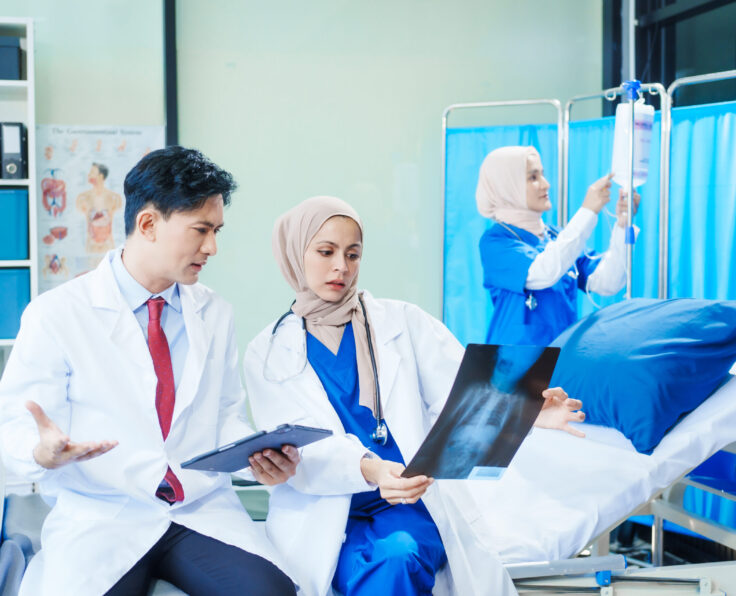 Two Muslim female doctors meet with an Asian male doctor to discuss an X-ray, blood vessel samples